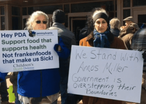 Two rally attendees are holding signs showing support for Amos Miller, an Amish Farmer
